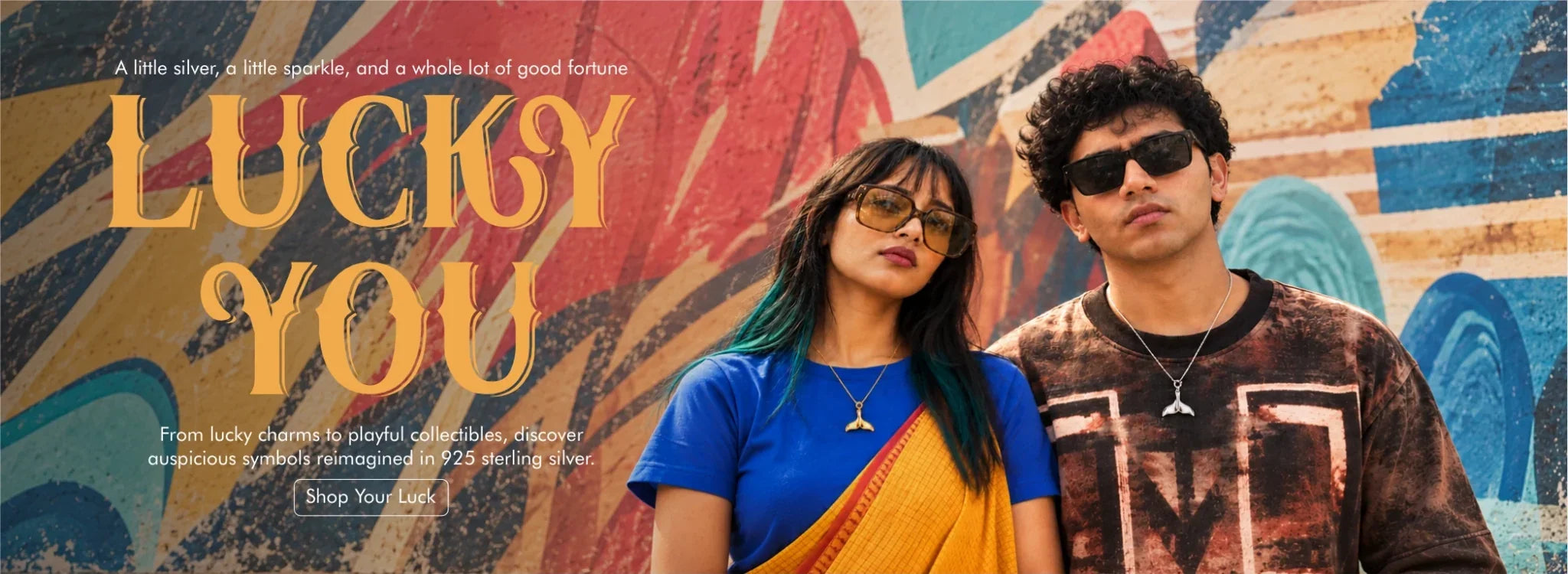 Lucky You collection: couple wearing silver and gold whale tail pendants against a painted wall