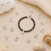 Black beaded bracelet with silver letter charms on a beige surface with scattered letter charms.