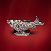 Silver Matsya fish idol on a beaded oval base, red backdrop